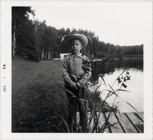 Boy in a cowboy hat standing beside Wabana Lake in July 1958