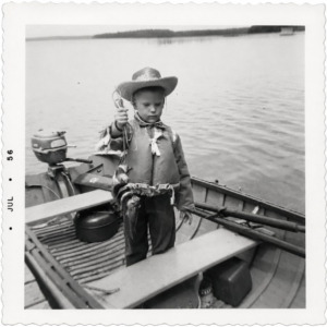 Child in a cowboy hat holding fish in a boat in July 1956