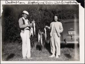 Couple displaying their fishing catch beside a vintage automobile