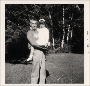 Adult holding a young child outdoors at WA-GA-THA-KA in August 1958